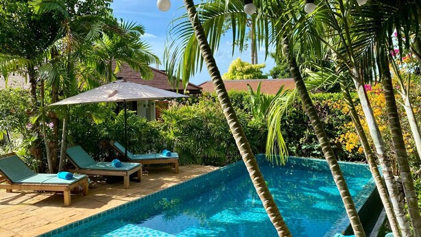 Una piscina con agua cristalina y azul, rodeada por una terraza de madera y sillones de descanso.