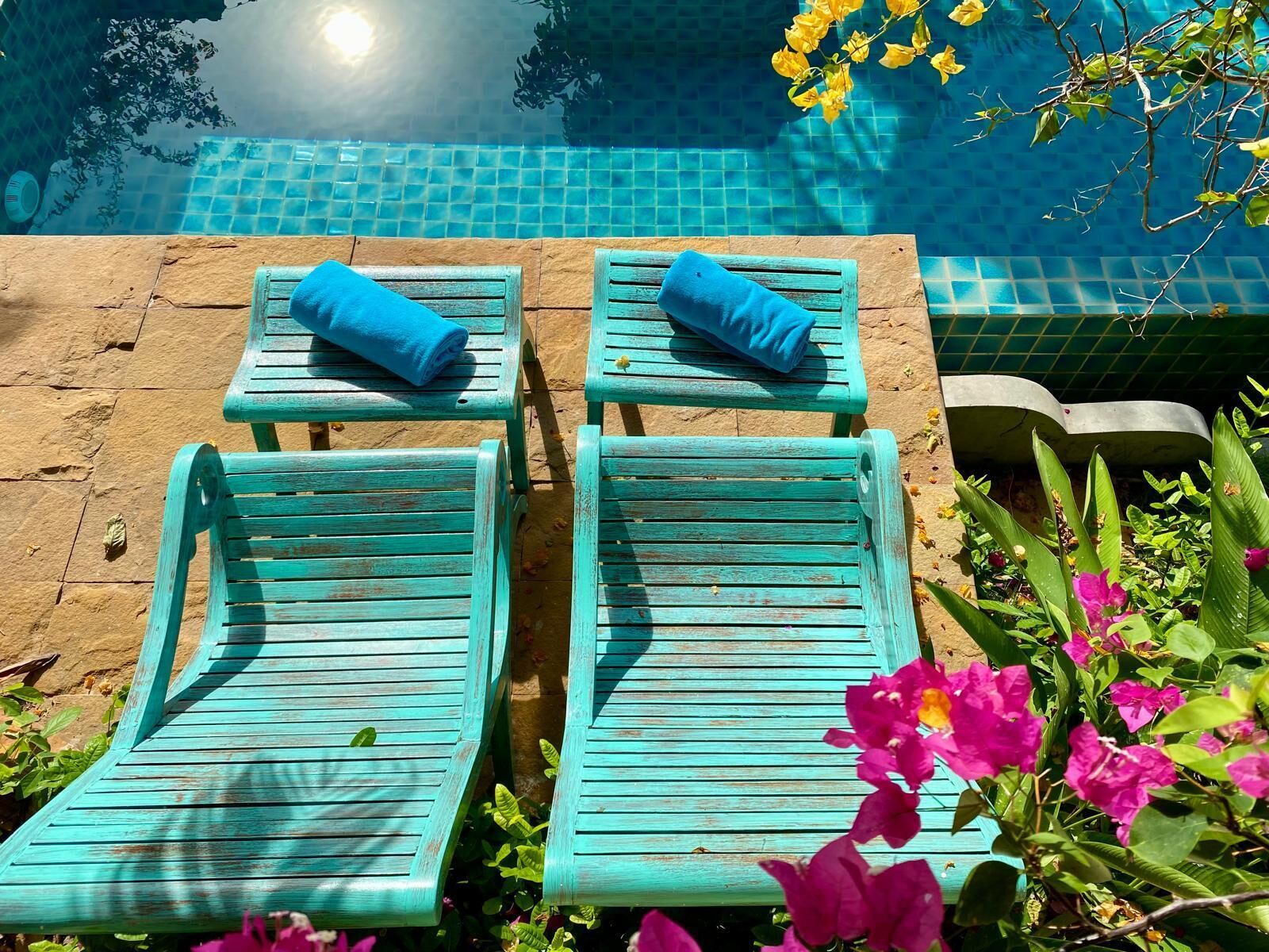 Un espace aménagé au bord de la piscine, avec quatre chaises longues turquoise, chacune agrémentée d’une serviette bleue.