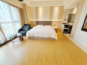 Moderni hotellihuone, jossa on suuri sänky, tuoli, yöpöytä ja suuri ikkuna, jossa on verhot.