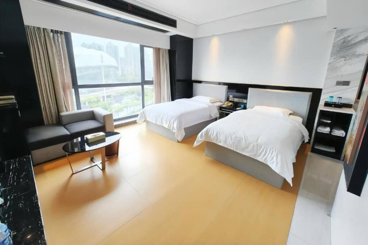 Una habitación de hotel moderna con dos camas, un sofá, una mesita y vistas a la ciudad.