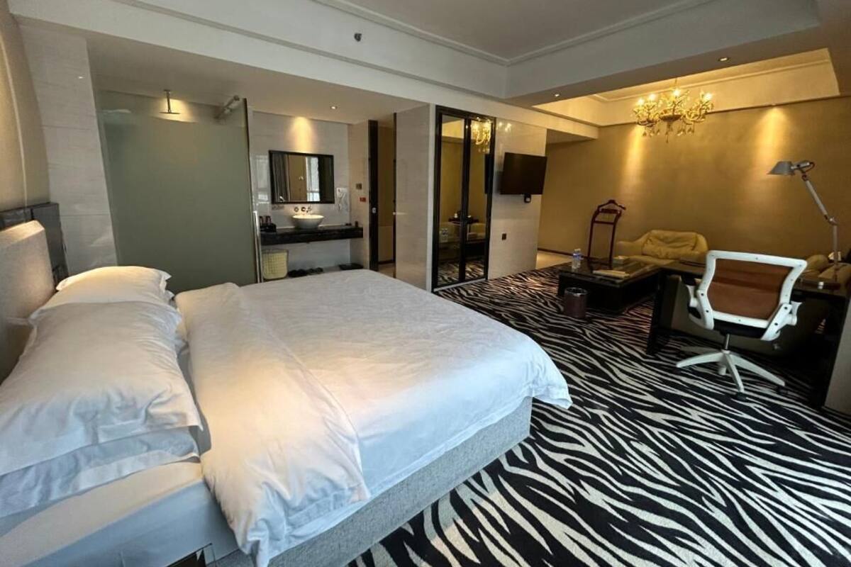 Una habitación de hotel con una cama grande, un escritorio, una silla, un espejo, un televisor y una araña.