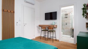 Una camera da letto con un letto, una TV, una scrivania con due sedie e uno spazio doccia.
