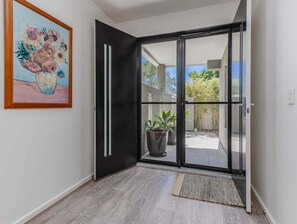 A modern interior with a sliding glass door leading to a balcony with potted plants. - Longboard Coastal Retreat (Tweed)