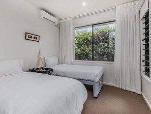 Ein Schlafzimmer mit zwei Betten, einem Fenster mit Vorhängen, einer Klimaanlage und einem gerahmten Bild an der Wand.