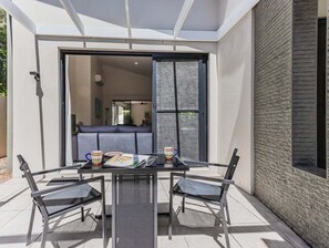 Eine Terrasse im Freien mit einem Glastisch und Stühlen, einer Couch und einer Glasschiebetür zu einem Innenraum.