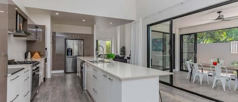 A modern kitchen with a large island, built-in appliances, and a dining area with outdoor seating.