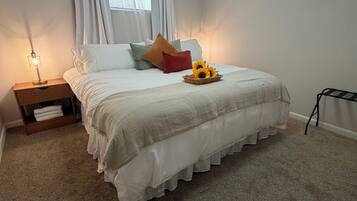 Un dormitorio con cama, mesita de noche, ventana con cortinas y una pequeña mesa con lámpara.