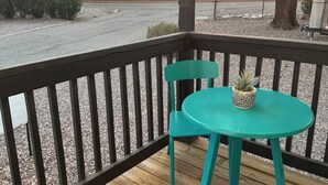 Una terraza de madera con una mesa y sillas turquesa, con vistas a un paisaje montañoso.