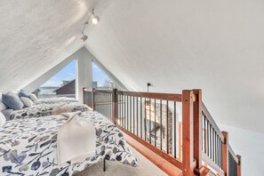 A bedroom with a sloped ceiling, a bed with patterned bedding, a wooden railing, and a view of a brick structure outside. - The Lakeview Loft at Bridges Bay Resort - Lakeview - 6 Waterpark Passes (Arnolds Park)