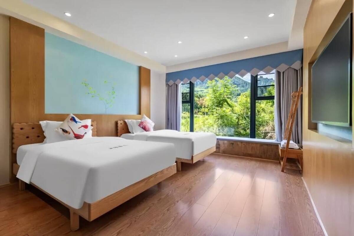 Habitación de hotel con dos camas, un ventanal con vistas, un cuadro en la pared y un televisor.