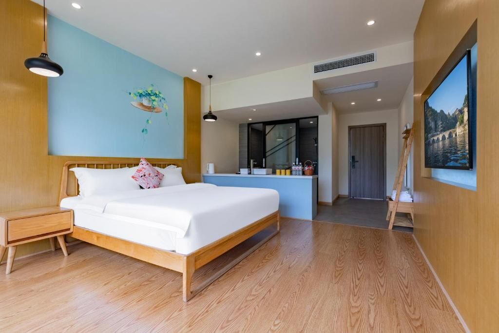 A modern bedroom with a wooden bed, a small bedside table, a blue accent wall, a painting, and a view of a staircase leading to a balcony.