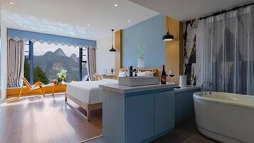 A modern hotel room with a bed, a small desk, a bathroom with a bathtub, and a view of mountains through a window.