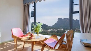 Ein Zimmer mit einem großen Fenster, einem runden Tisch, zwei Stühlen und einer Vase mit Blumen.