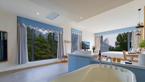 Ein modernes Badezimmer mit einer großzügigen Badewanne, einem Waschbecken und einem Spiegel. Ein Fenster mit Vorhängen bietet Blick auf Bäume und Berge.