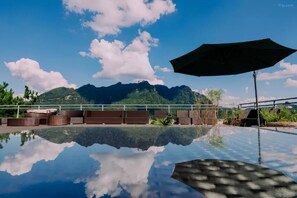 A clear pool with a mountain view, lounge chairs, and an umbrella. - Zhangjiajie Peak & Cloud Retreat (Zhangjiajie)