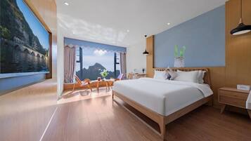 Una habitación de hotel moderna con una cama grande, piso de madera, vistas a un paisaje montañoso y una pequeña mesa con sillas.
