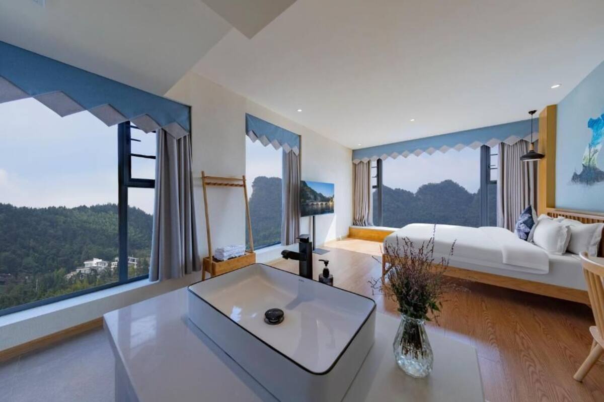 Un hotel moderno con una ventana grande, una mesita de noche, un sofá blanco y un cuadro en la pared.