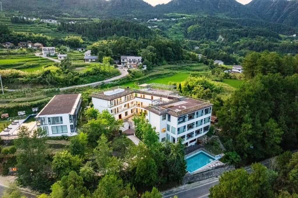 Un edificio moderno de varios pisos con piscina en la azotea, rodeado de exuberante vegetación y terreno montañoso.