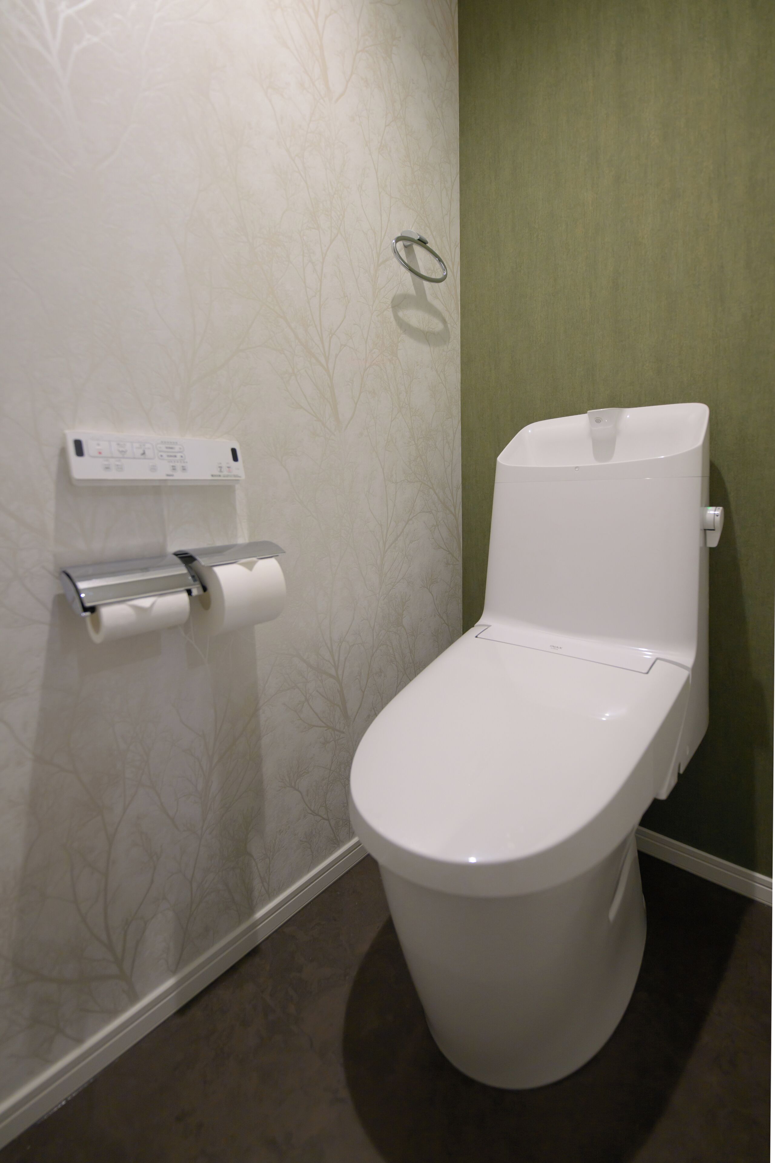 A toilet with a paper towel dispenser, a flush handle, and a wall-mounted flush button.