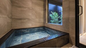 A modern bathroom with a glass-enclosed bathtub, a window with a view of greenery, and a door with a handle. - TEMARI Premier NORTH (Hakone)