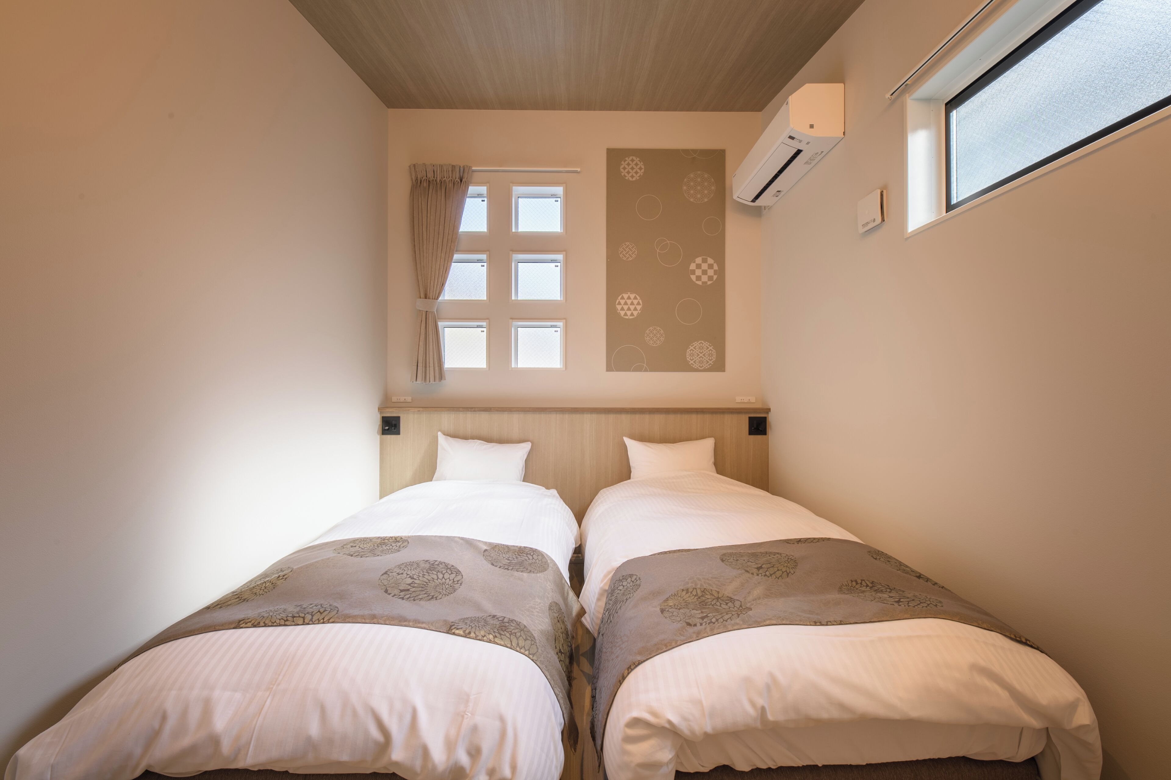 A twin room with two beds, a window, an air conditioning unit, and a wall-mounted artwork.