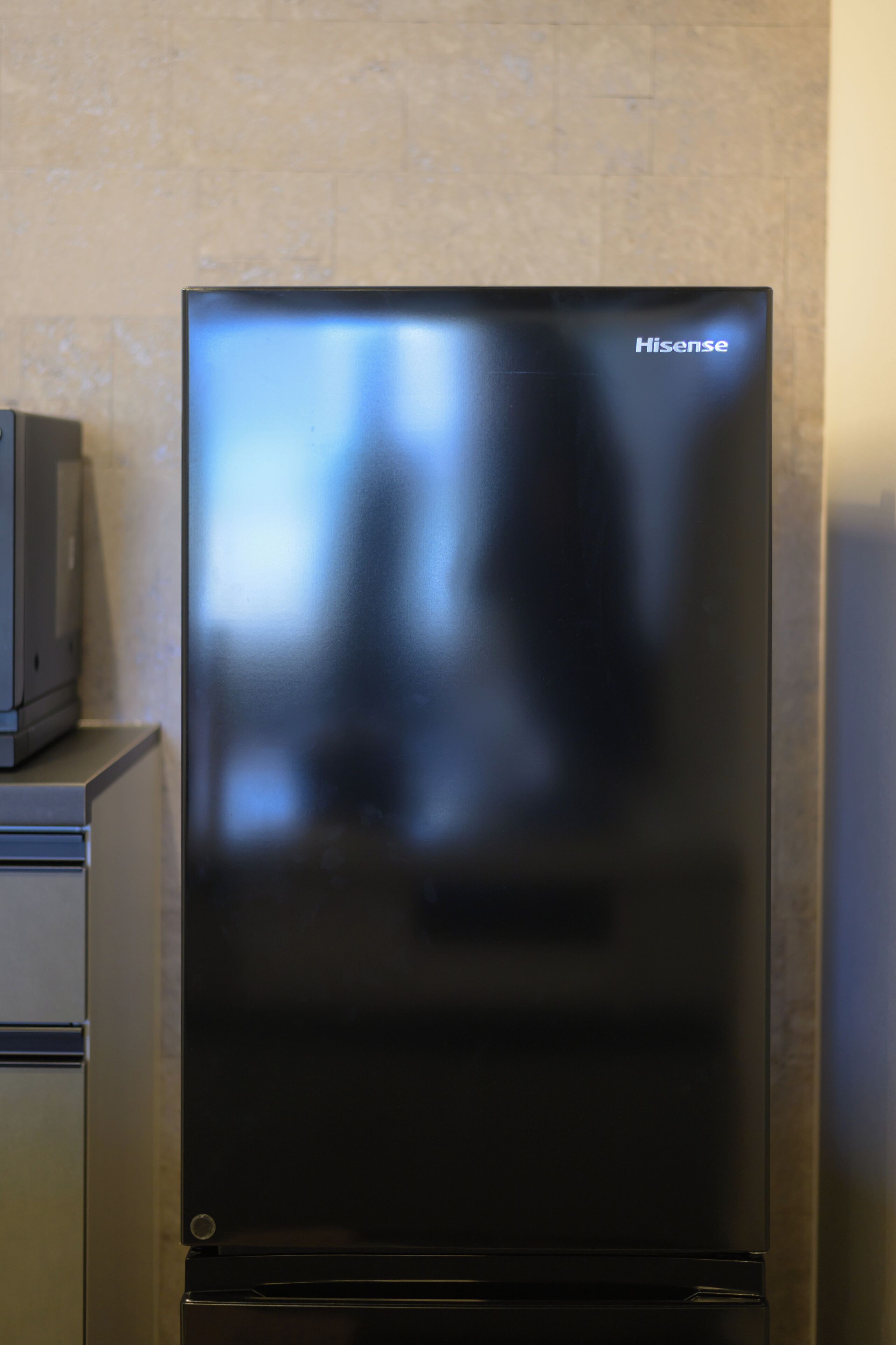A black Hisense refrigerator with a digital display, placed against a tiled wall.