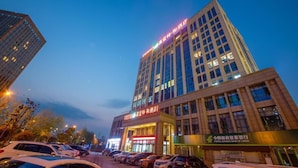 A multi-story building with illuminated signage, a parking lot, and a storefront with a sign in a foreign language. - Friend Zhangjiajie Hotel (Zhangjiajie)