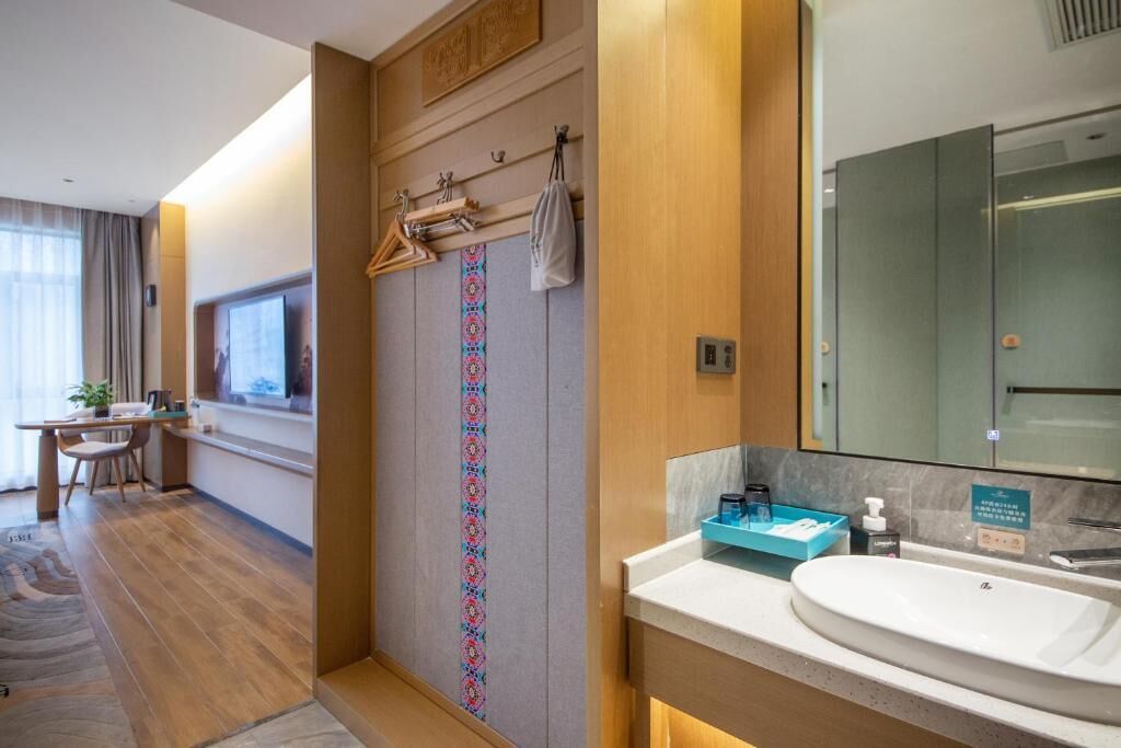 A modern hotel room with a wooden floor, a large mirror, a sink, and a shower area.