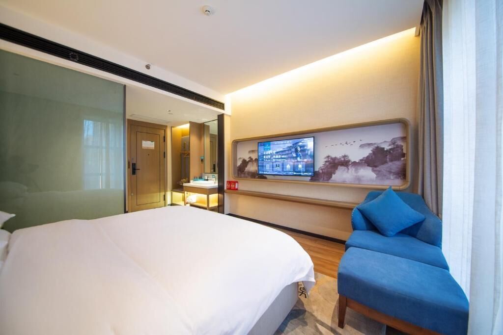 Une chambre d’hôtel avec un lit, un bureau équipé d’un ordinateur, une chaise bleue et un téléviseur fixé au mur.