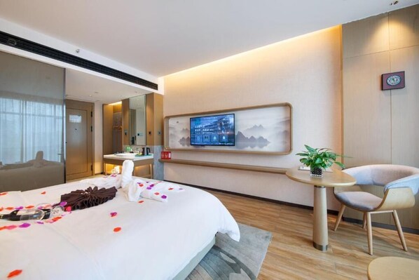 Habitación de hotel con cama, televisor montado en la pared, una mesita con una planta y una silla.