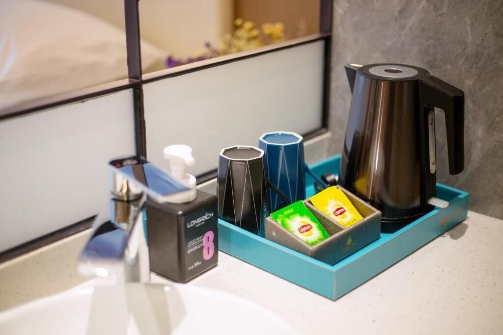 A hotel bathroom with a mirror, a sink, a coffee maker, a tissue dispenser, and a soap dispenser.