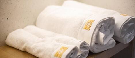 A set of neatly folded white towels with a gold emblem on a wooden shelf.
