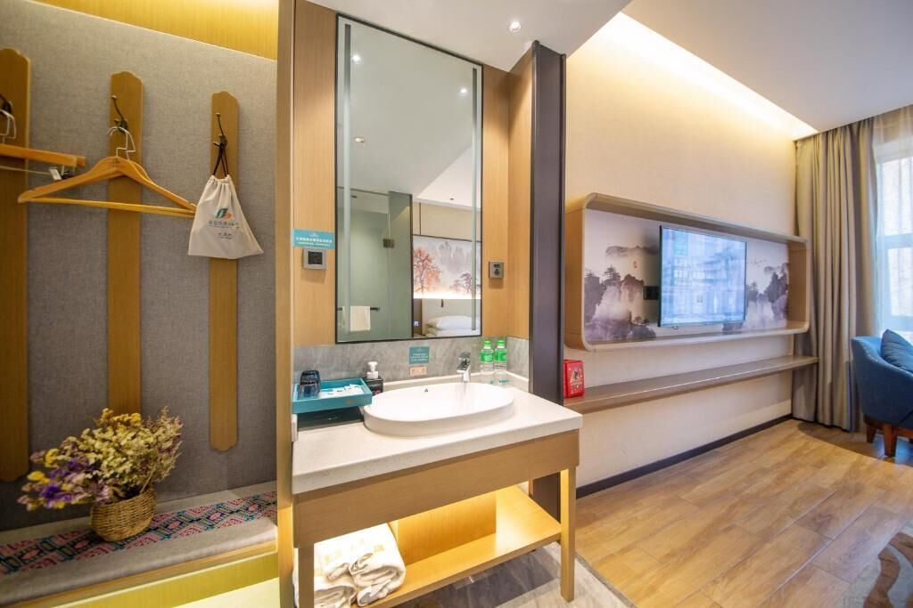 A modern hotel bathroom with a sink, mirror, towel rack, and a television on the wall.