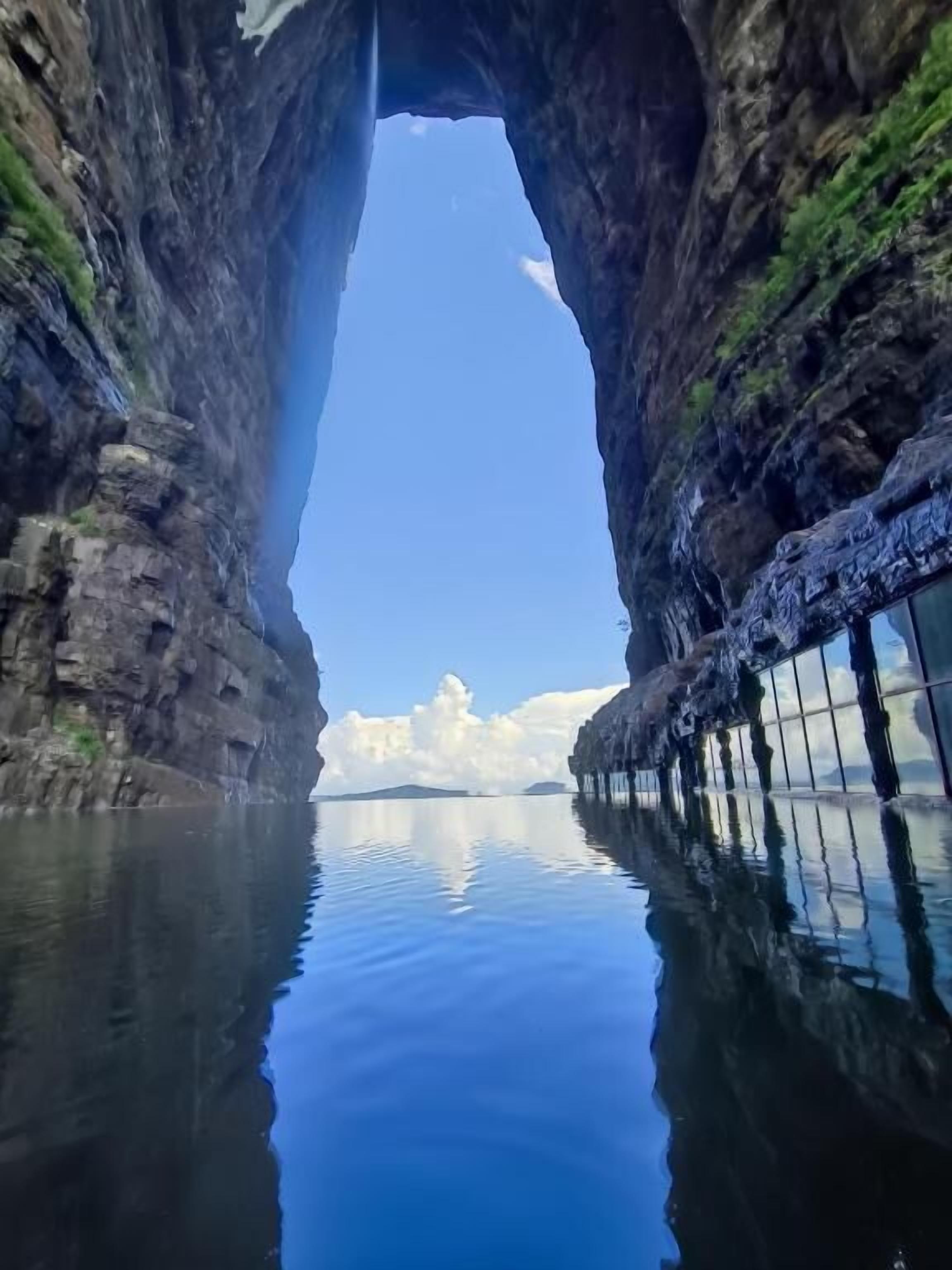 A clear view through a natural rock arch into a calm body of water with a distant island.