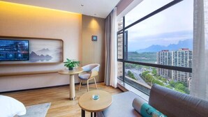 A modern hotel room with a large window, a flat-screen TV, a sofa, a small table, and a chair. - Friend Zhangjiajie Hotel (Zhangjiajie)