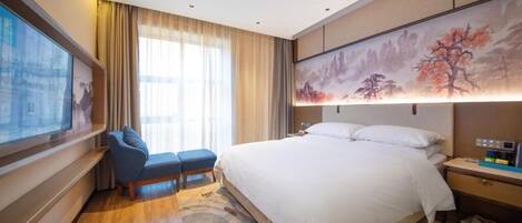 A hotel room with a bed, a chair, a desk, a large window, and a painting on the wall.