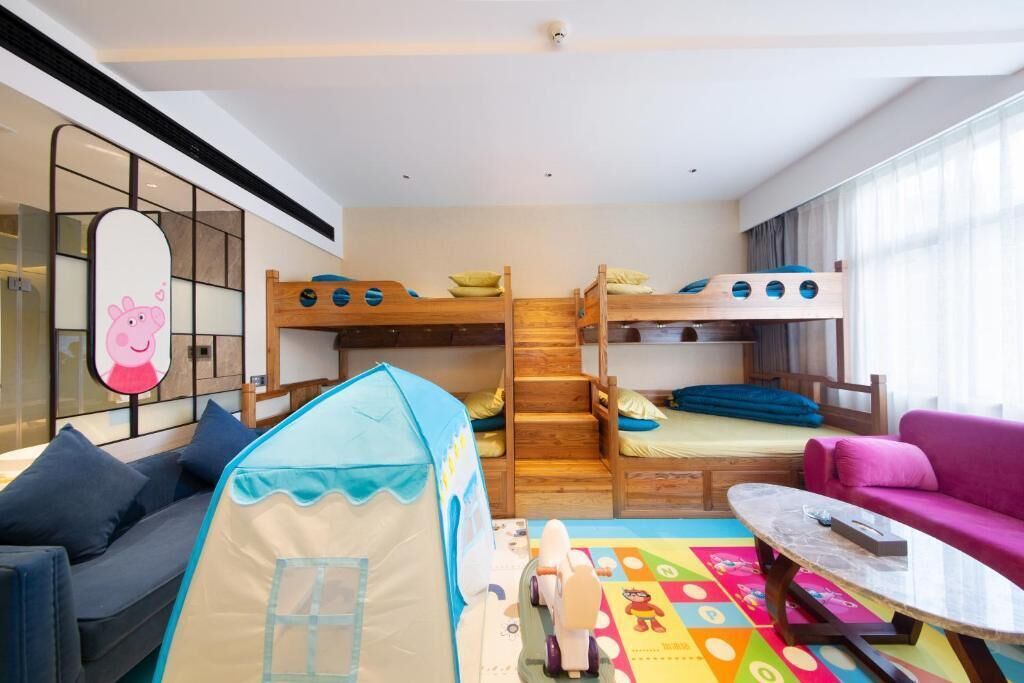 A children's room with bunk beds, a play tent, a colorful play mat, a sofa, and a table.