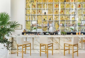 A bar area with a marble countertop, three white bar stools, and a wall of shelves with various bottles. - Villa La Valencia Beach Resort & Spa Los Cabos (San José del Cabo)