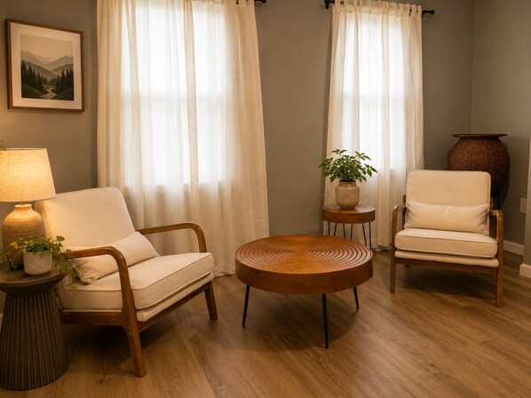 A living room with a sofa, armchair, round coffee table, and a lamp on a side table.