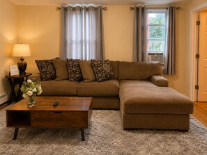 A living room with a brown sectional sofa, a wooden coffee table, a lamp, and a vase with flowers.