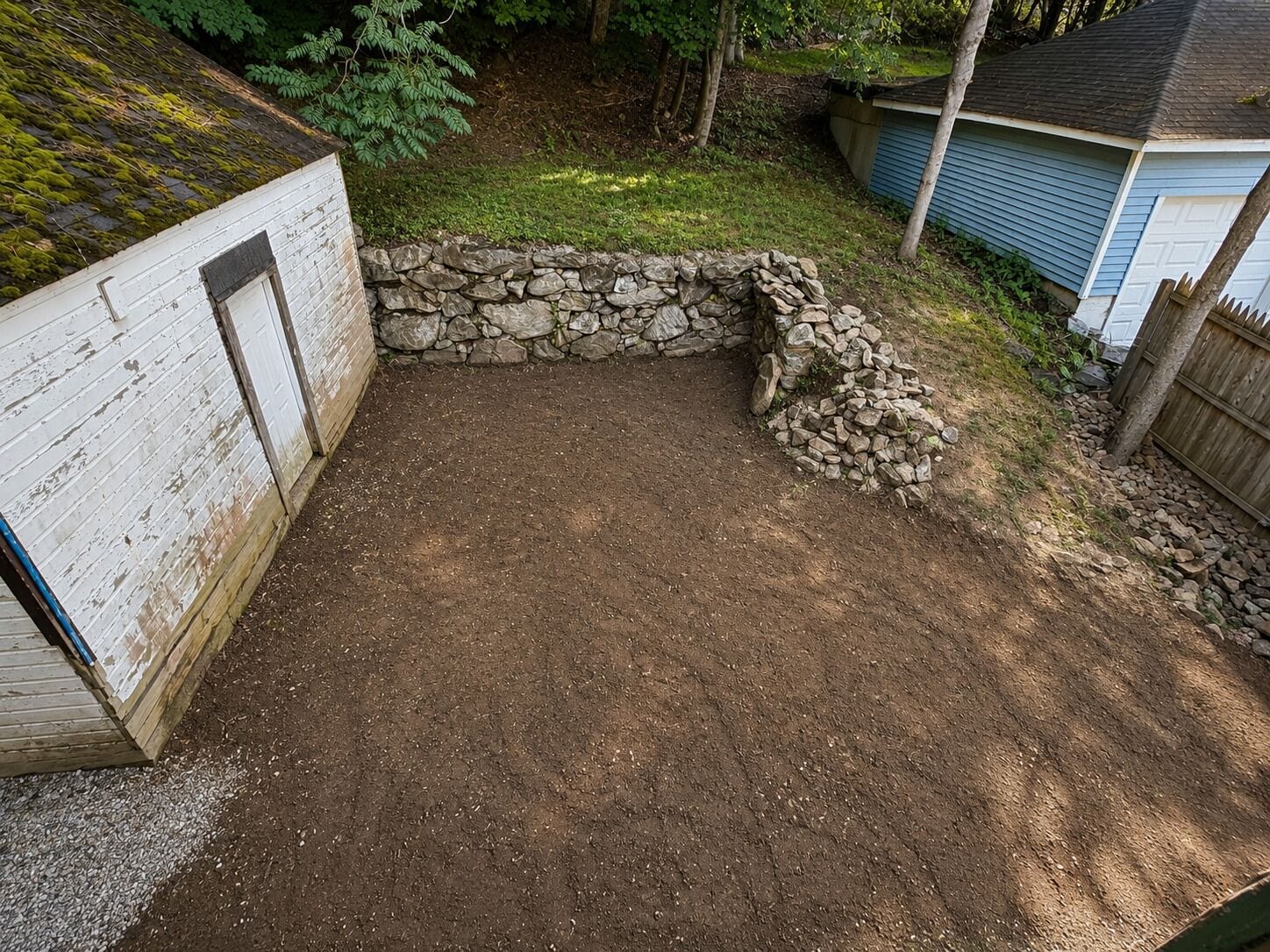 A dirt patio area with a stone wall and a wooden fence.
