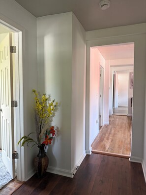 A hallway with wooden flooring, white walls, and a door on the left.