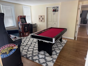 A pool table with a red felt surface, a pool cue, and a corner billiards table. - Modern 2BR Getaway with Arcade Game Room &  Lounge Near Mohegan Sun & Foxwoods (Norwich)