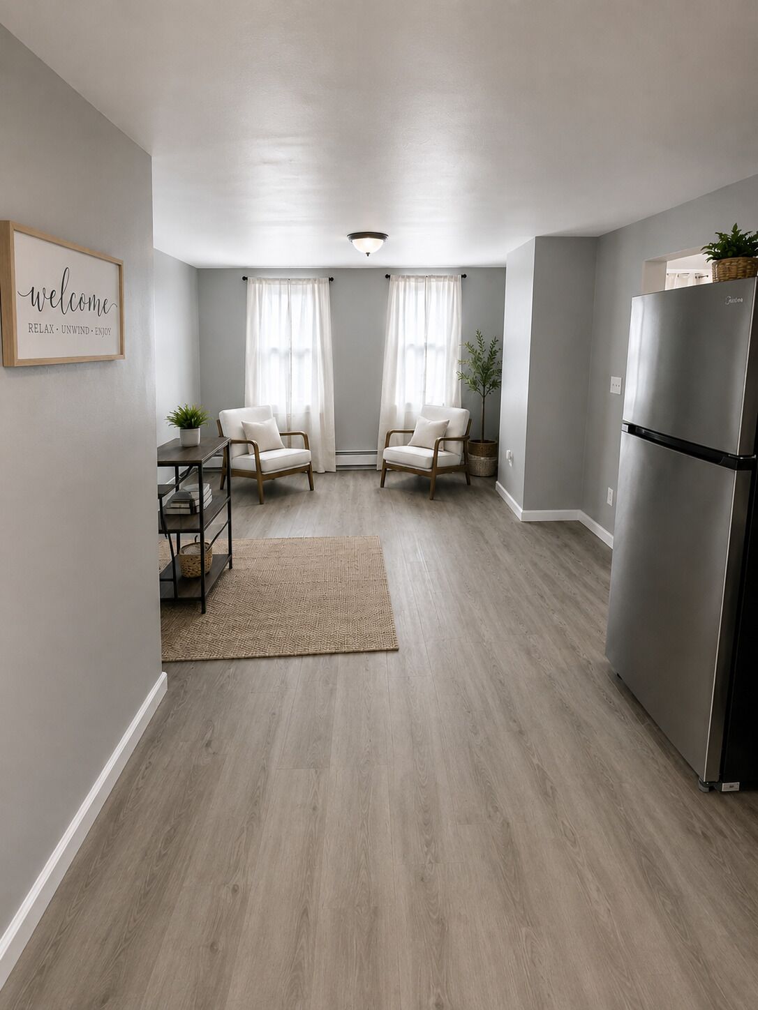 A modern kitchen with a built-in refrigerator, two white chairs, a small table with a plant, and a welcome sign on the wall.