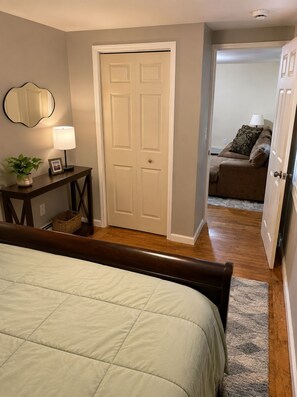A bedroom with a bed, bedside table, lamp, and a door leading to another room.