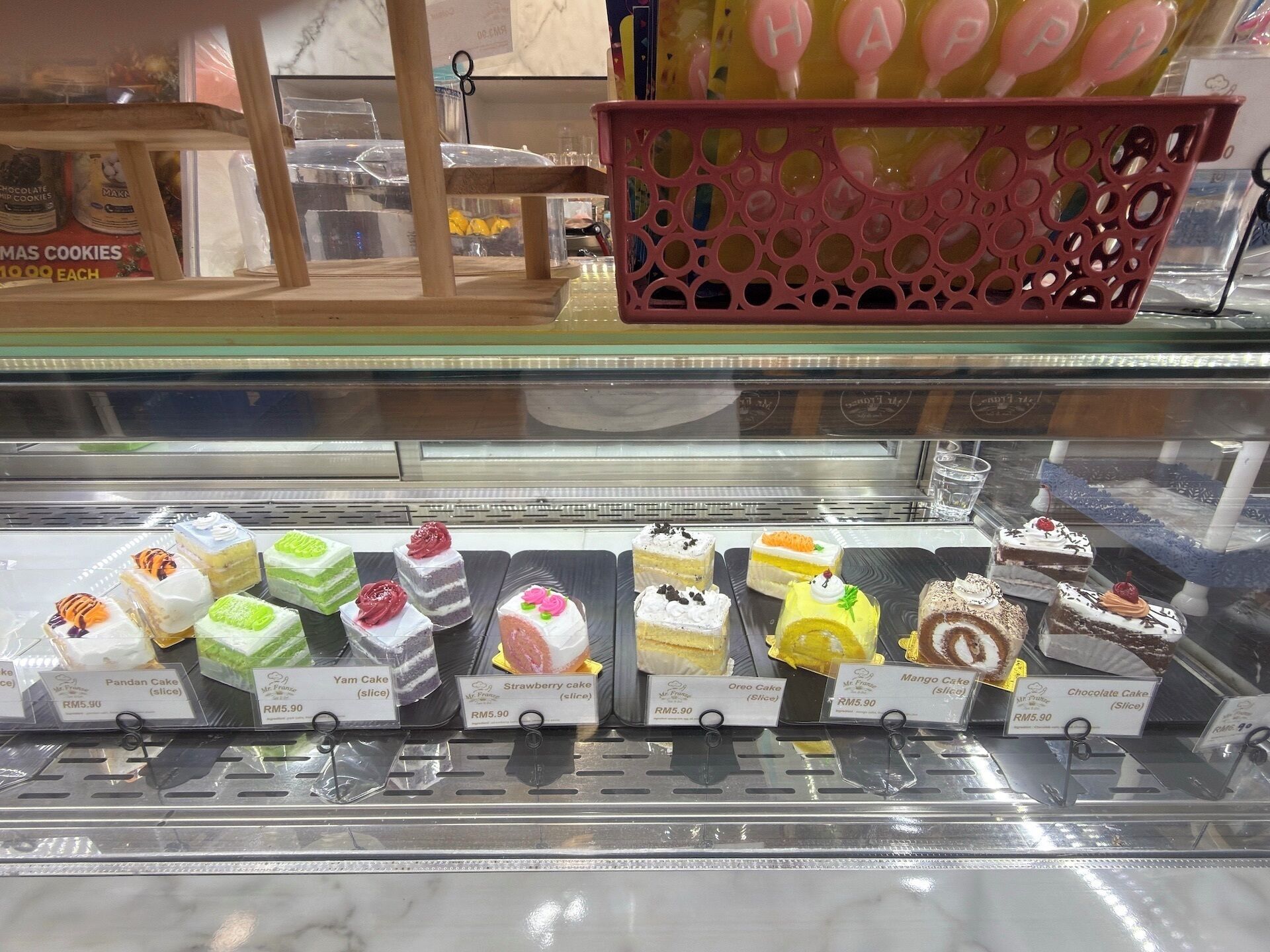 Vitrina de pastelería con diversos pasteles y productos de repostería, cada uno con su precio indicado.