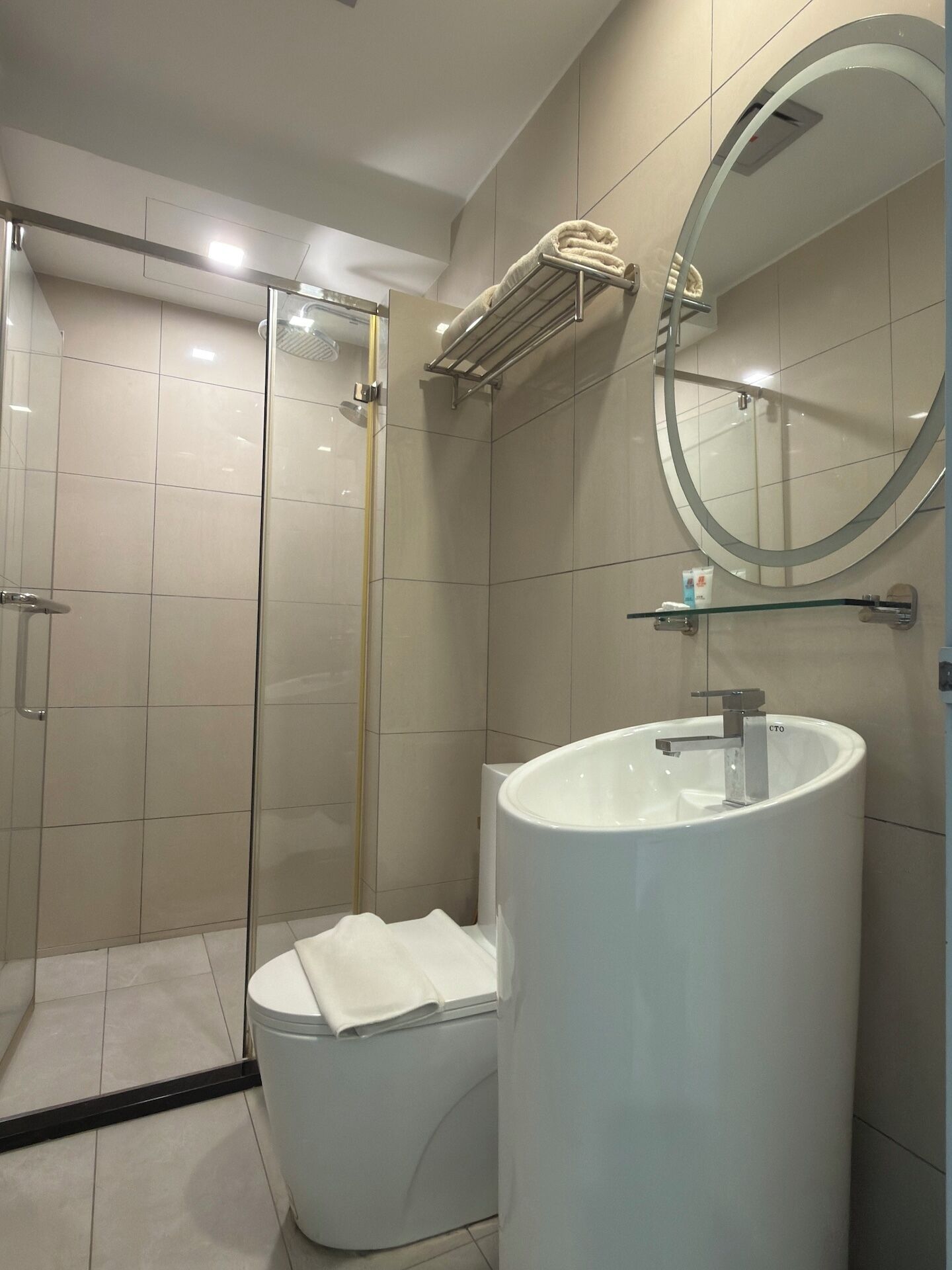 A modern bathroom with a glass-enclosed shower, a large sink, and a round mirror.