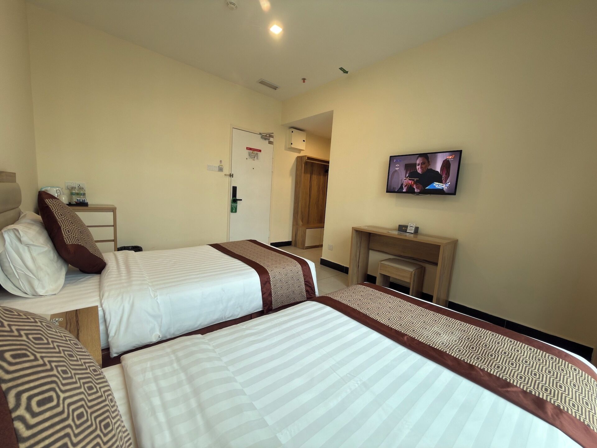 A hotel room with two beds, a television, a desk, and a door.