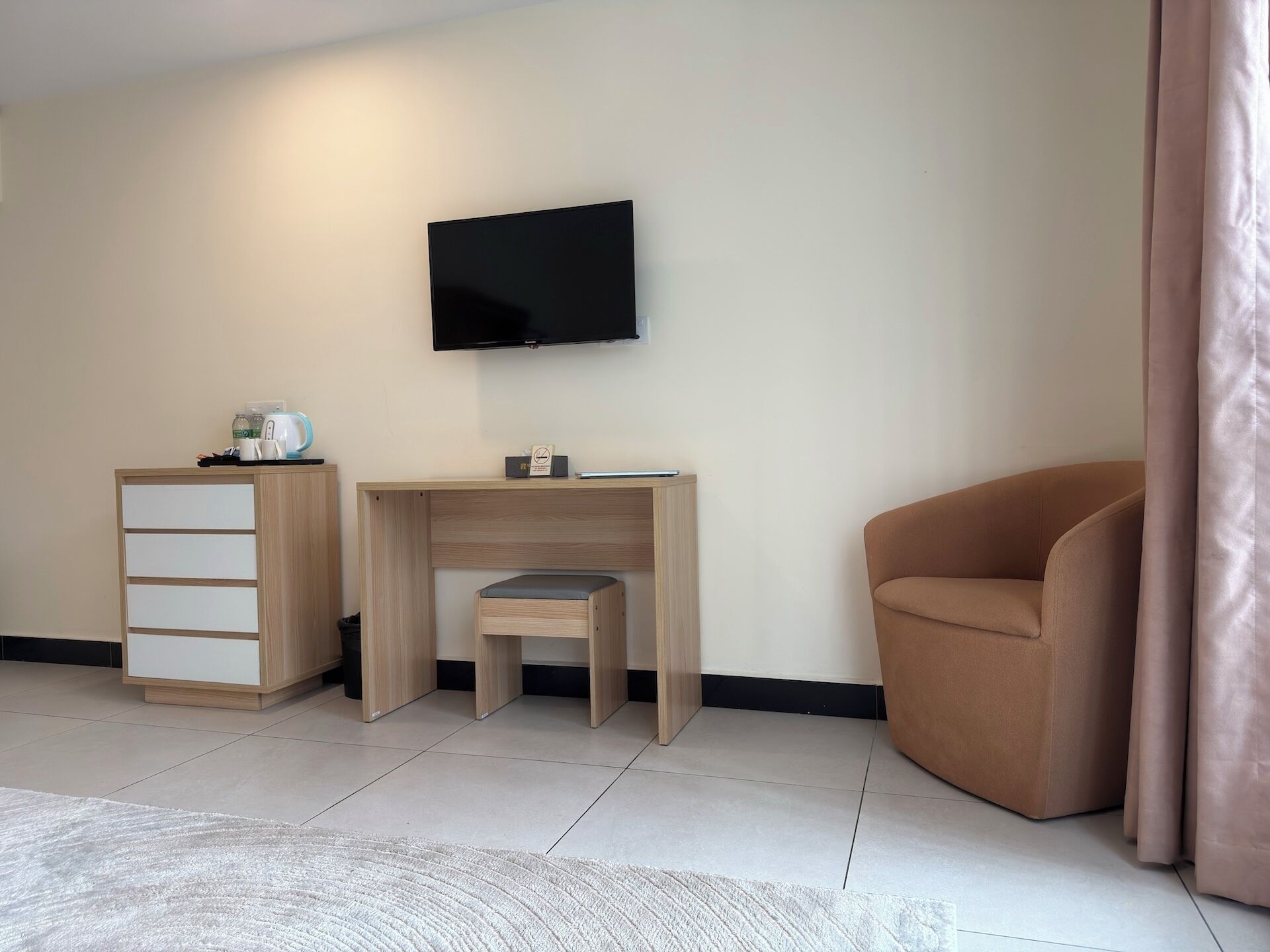 Una habitación moderna con un escritorio de madera, un televisor, una silla marrón y una alfombra blanca.