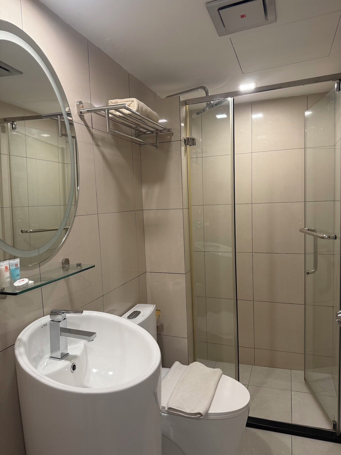 A modern bathroom with a glass-enclosed shower, a round mirror, and a white sink.